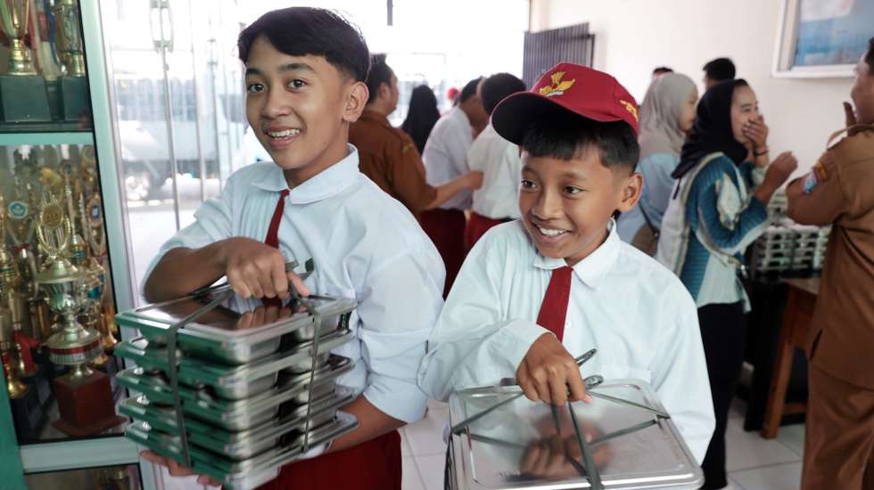 epaselect epa11808204 Elementary school students carry food trays at Lengkong 1 elementary school in Tangerang, Indonesia, 06 January 2025. The Indonesian government has officially started the Free Nutritious Meal Program (MBG) with a total of 190 kitchens across 26 provinces serving the community, aiming to make a major milestone in fulfilling national nutrition needs.  EPA/ADI WEDA