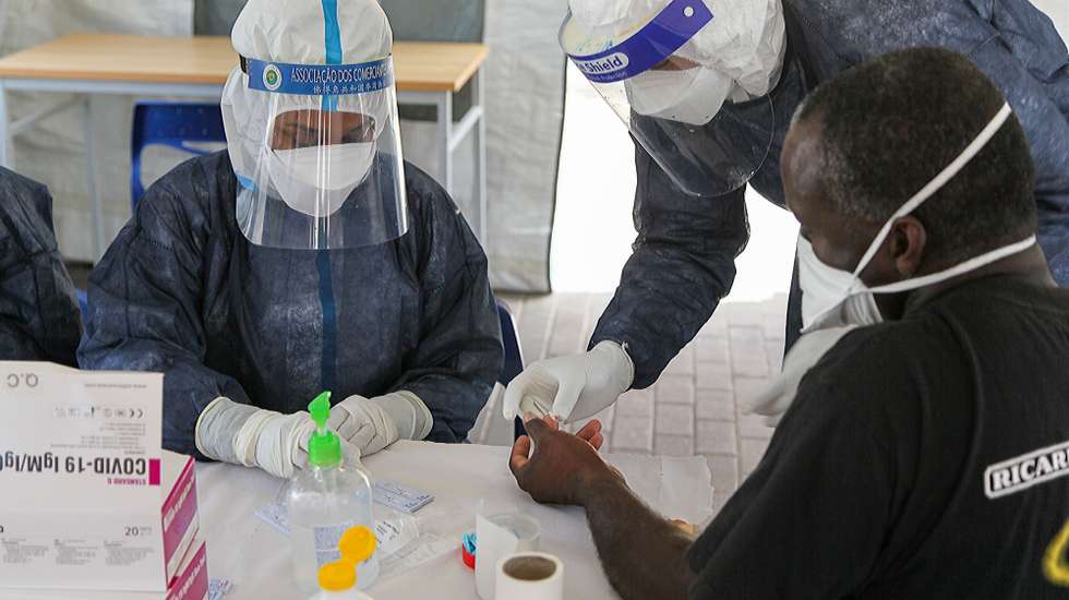 Profissional da saúde, totalmente equipado com vestuário de proteção contra a covid-19, recolhem uma amostra de sangue de um popular durante a realização de testes gratuitos à presença do novo coronavírus na população, numa tenda de campanha instalada num bairro da cidade da Praia, organizada pelas autoridades de saúde e proteção civil, e realizada pela Cruz Vermelha de Cabo Verde, com apoio da polícia e militares, Cabo Verde, 23 de maio de 2020. Tendas instaladas nos bairros da cidade da Praia estão a permitir a realização de testes rápidos em massa à presença do novo coronavírus na comunidade, para alívio da população, confrontada com o foco da pandemia na capital cabo-verdiana. (ACOMPANHA TEXTO). FERNANDO DE PINA/LUSA