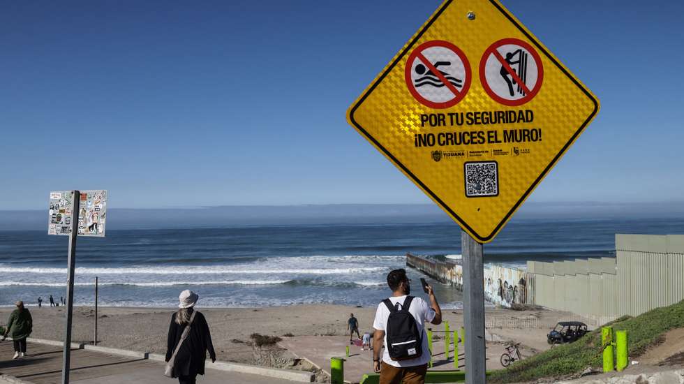epa11047431 People walk next to a security notice for migrants in the border beach of Tijuana, Mexico, 27 December 2023 (issued 28 December 2023). Irregular migrant crossings in Tijuana, one of Mexico's main borders with the United States, have grown by 31 percent annually to exceed 230,000 this year, prompting municipal authorities to warn about the growing dangers undocumented people face.  EPA/Joebeth Terriquez