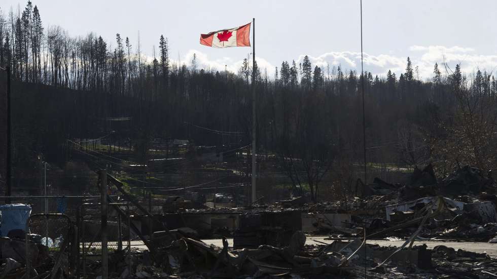 epa05309303 A handout picture made available by the Government of Alberta on 16 May 2016 shows a Canadian national flag flying over a general view of damage caused by a wildfire that swept through several neighbourhoods in Fort McMurray, Alberta, Canada, 14 May 2016. Alberta Health Services has issued an air-quality advisory for the Fort McMurray area. A wildfire erupted on 03 May destroying the city of Fort MacMurray, and forcing more than 88,000 people to evacuate from the area, leaving more than 200,000 hectares burnt. Government officials say that only heavy rain would extinguish the fire.  EPA/GOVERNMENT OF ALBERTA/CHRIS SCHWARZ  HANDOUT EDITORIAL USE ONLY