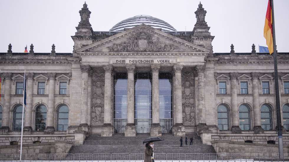 epa08916452 A woman with an umbrella passes by the Reichstag building during snowfall in Berlin, Germany, 03 January 2021. Media reports state, that up to 5 centimeters fresh snow might be expected.  EPA/CLEMENS BILAN