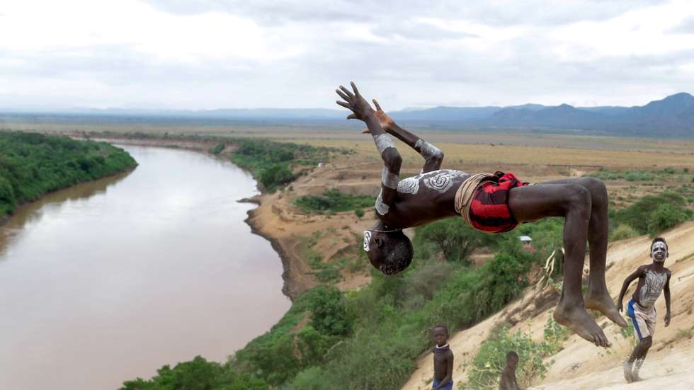 epa07909555 A child from the Kara (or Karo) tribe in southern Ethiopia, jumps at the edge of a cliff along the Omo River, in Kolcho, Ethiopia, 26 September 2019 (issued 10 October 2019). The tribe has an estimated population of about 2,000 people scattered in different villages, making them the smallest ethnic group in southern Ethiopia. They live along the Omo River and mainly live on agriculture and fishing. When preparing for ceremonies such as wedding days the tribespeople paint their bodies and faces with chalk mixed with water.  EPA/STEPHANIE LECOCQ  ATTENTION: This Image is part of a PHOTO SET