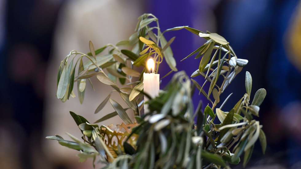 epa09894263 A Lebanese Orthodox Christian carries a candle with an olive branch during a Palm Sunday mass at the Saint George Cathedral in downtown Beirut, Lebanon, 17 April 2022. Palm Sunday for Christian Orthodox devotees symbolically marks the entry of Jesus Christ into Jerusalem, signaling the start of the Holy Week before Easter.  EPA/WAEL HAMZEH