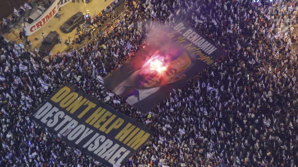 epaselect epa10658297 A flare lights a banner depicting Israeli Prime Minister Benjamin Netanyahu, carried by anti-government protesters during a protest against the justice system reform in Tel Aviv, Israel, 27 May 2023. Mass protests against the government's justice system reform plan continue across the country. Protesters have been calling for the reforms to be scrapped and for Prime Minister Benjamin Netanyahu to resign.  EPA/ABIR SULTAN