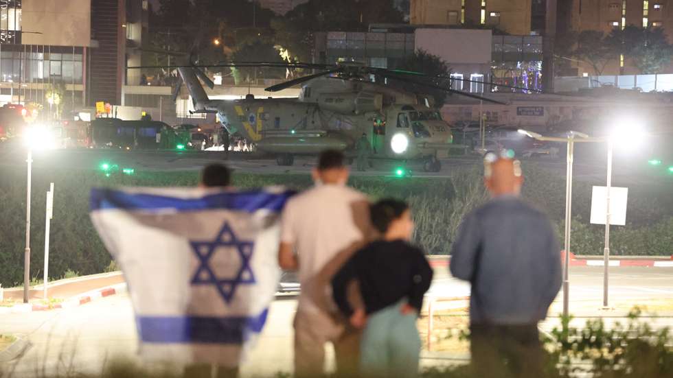 epa10993393 People with an Israeli flag looks on as an Israeli army helicopter carrying Israeli children hostages who were held by Hamas in Gaza, landed at the helipad of the Schneider-Children's Medical Center in Petah Tikva, Israel, 24 November 2023. Israel and Hamas agreed to a four-day ceasefire agreement, mediated by Qatar, the US, and Egypt, that came into effect at 05:00 AM GMT on 24 November, with 50 Israeli hostages, women and children, to be released by Hamas and 150 Palestinian women and children that were detained in Israeli prisons to be released in exchange. More than 14,000 Palestinians and at least 1,200 Israelis have been killed, according to the Gaza Government media office and the Israel Defense Forces (IDF), since Hamas militants launched an attack against Israel from the Gaza Strip on 07 October, and the Israeli operations in Gaza and the West Bank which followed it.  EPA/ABIR SULTAN
