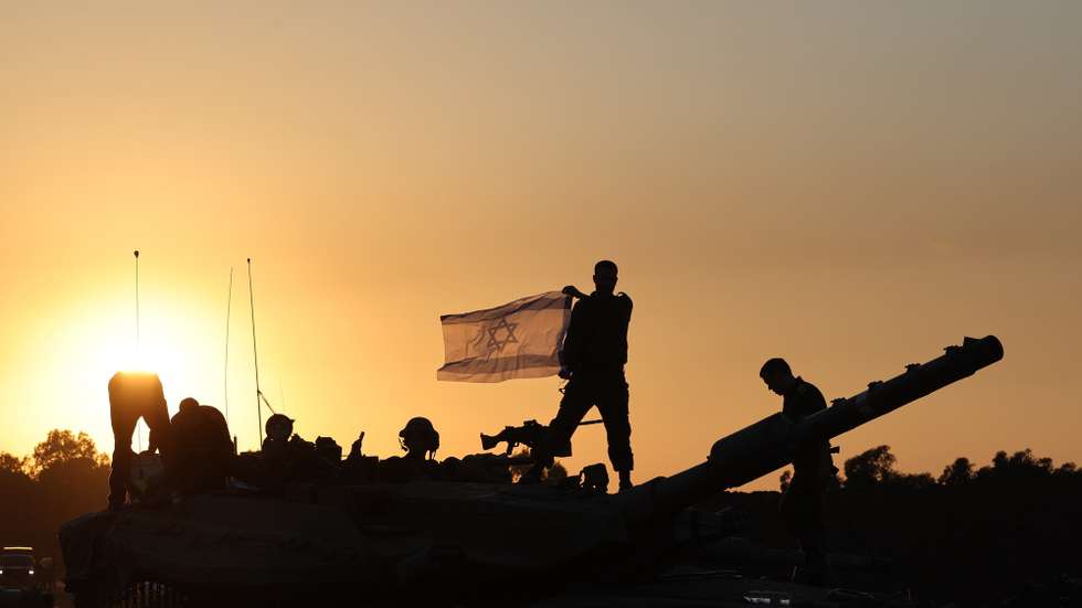 epa11001466 An Israeli soldier holds an Israeli flag while standing on top of a tank during a temporary ceasefire, near the Gaza border, in southern Israel, 29 November 2023. A four-day ceasefire agreed by Israel and Hamas was extended by 48 hours on 27 November, as more talks on a possible extension were ongoing. The Israeli army on 29 November reissued its daily message to the residents of Gaza to avoid moving back into northern Gaza which is considered a 'war zone', to not approach within one kilometer of the border and to not access the sea. Thousands of Israelis and Palestinians have died since the militant group Hamas launched an unprecedented attack on Israel from the Gaza Strip on 07 October, and the Israeli strikes on the Palestinian enclave which followed it.  EPA/ABIR SULTAN