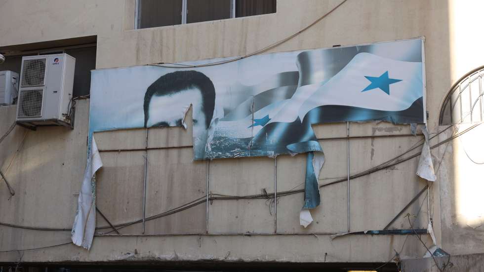 epaselect epa11765465 A torn banner depicting the picture of Bashar al-Assad on a building after rebels took over Damascus, Syria, 08 December 2024. Syrian rebels entered Damascus on 08 December 2024 and announced in a televised statement the 'Liberation of the city of Damascus and the overthrow of Bashar al-Assad,' as well as the release of all the prisoners. The rebels also urged the Syrian armed forces to leave Syrian public institutions, which will stay under the control of the outgoing Syrian prime minister until the official handover ceremony  EPA/MOHAMMED AL RIFAI