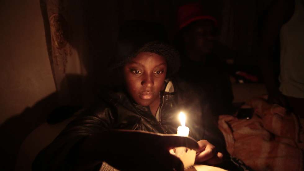 epa10096477 Ruvimbo Makombe uses a candle amid power cut in Harare, Zimbabwe, 28 July 2022. According to economists, Zimbabwe could miss its economic growth targets for the first quarter of this year due to losses in production time if power cuts persist. As a result of load shedding many businesses have reverted to alternative power sources, such as fuel-powered generators, which have become even more expensive to operate.  EPA/AARON UFUMELI