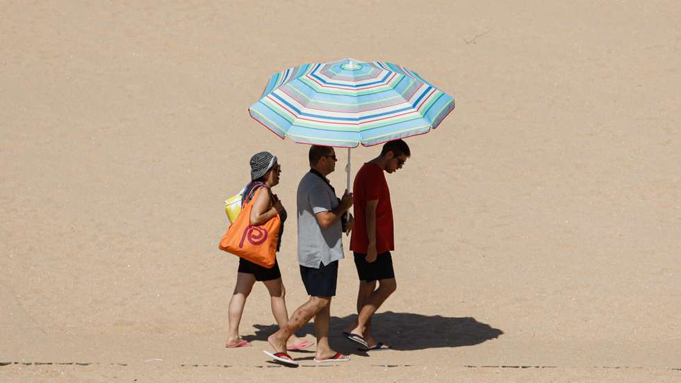 Turistas protegem-se do sol com um guarda-sol numa praia em Albufeira, 22 de agosto de 2023. Por causa do tempo quente, o IPMA colocou os distritos de Vila Real, Bragança, Viseu, Guarda, Coimbra, Castelo Branco e Santarém sob aviso vermelho entre as 00:00 de hoje e as 10:00 de quinta-feira. LUÍS FORRA/LUSA