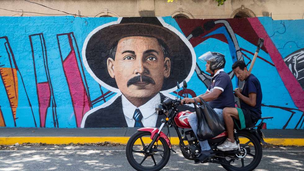 epa11924405 Two men on a motorcycle ride past a mural of Blessed Jose Gregorio Hernandez in Caracas, Venezuela, 25 February 2025. The Catholic Church of Venezuela celebrates the canonization of the Venezuelan blessed Jose Gregorio Hernandez Cisneros, approved by Pope Francis, making him the first saint of the Caribbean country.  EPA/RONALD PENA R