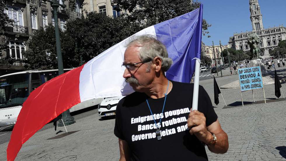 Um participante vestindo uma t-shirt com as palavras "Emigrantes Poupam, Bancos Roubam, Governo Deixa Andar" segura uma bandeira de França, durante a manifestação dos lesados do papel comercial e lesados imigrantes do Banco Espírito Santo (BES), à frente a uma agência do Novo Banco e do Banco de Portugal, na Avenida dos Aliados, no Porto, 19 de setembro de 2018. MANUEL FERNANDO ARAÚJO/LUSA