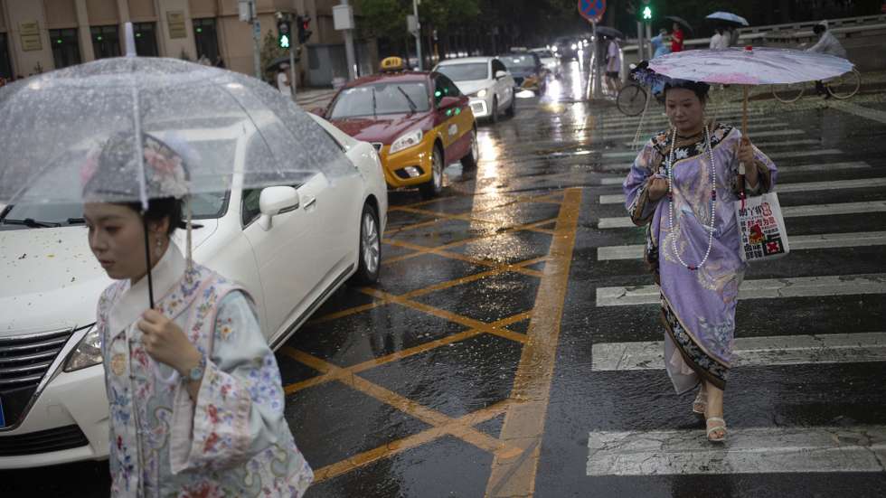 epa12233671 Women wearing traditional dresses carry umbrellas to protect themselves from rain while walking along a street of Beijing, China, 12 July 2025.  EPA/ANDRES MARTINEZ CASARES