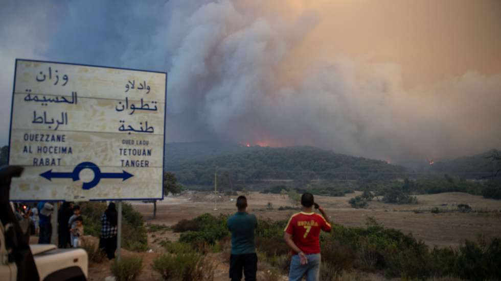 epa12296464 People watch as smoke rises from a forest fire in the Kranekha area near Chefchaouen, Morocco, 12 August 2025. The forest fire has spread towards the forests of Tanqub and Bab Taz driven by strong winds, prompting the intervention of Civil Protection teams, local volunteers and two Canadair fire fighting aircraft.  EPA/Jalal Morchidi