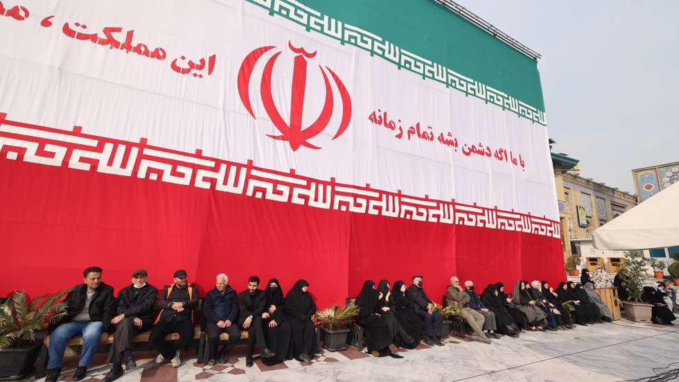 epa12819685 People and relatives of late Iranian supreme leader's top adviser Ali Shamkhani sit under a huge Iran national flag during a funeral ceremony at the Saleh shrine in Tehran, Iran,14 March 2026. A joint Israeli and US military operation continues to target multiple locations across Iran since the early hours of 28 February 2026.  EPA/ABEDIN TAHERKENAREH