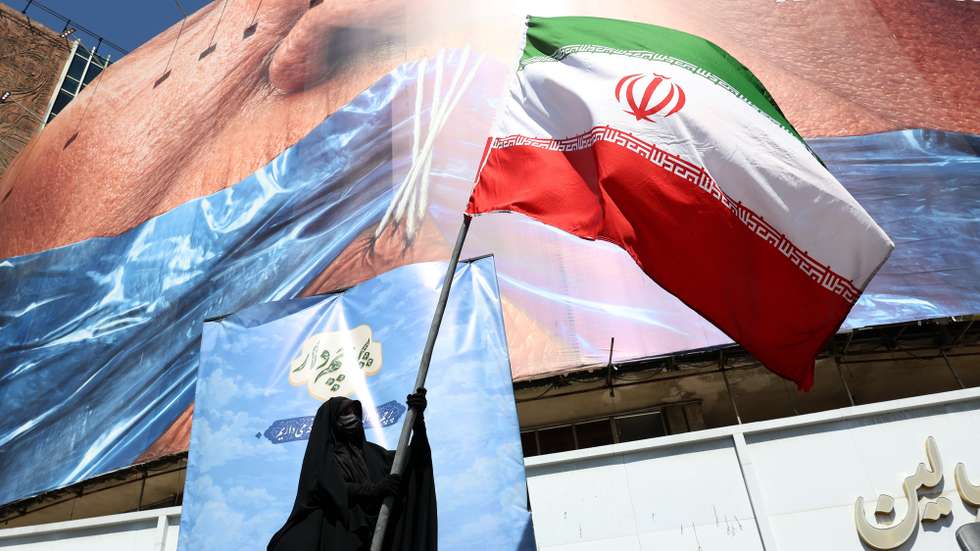epa12946980 A veiled woman holds Iran’s national flag in front of a huge anti-US billboard referring to US President Donald Trump and the Strait of Hormuz at Valiasr Square in Tehran, Iran, 11 May 2026. US President Donald Trump says Iran’s counter-proposal to end the ongoing conflict is not acceptable.  EPA/ABEDIN TAHERKENAREH