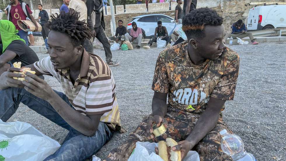 epa13150613 Migrants eat food distributed by the Red Cross personnel at El Trampolin beach in Ceuta, Spain, 04 August 2026. According to Spanish officials, around 2,500 migrants remain in Ceuta following last week's massive border rush from Morocco, with many living in overcrowded reception centers or sleeping outdoors on beaches and in parks.  EPA/REDUAN