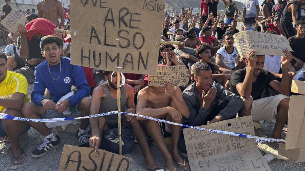 epa13176333 Migrants hold signs that read 'We are also human' and 'Asylum' during a hunger strike at the El Trampolin beach campsite in Ceuta, Spain, 17 August 2026. The migrants entered the Spanish enclave from Morocco during the mass border crossings that began on 30 July.  EPA/LAURA RINCON