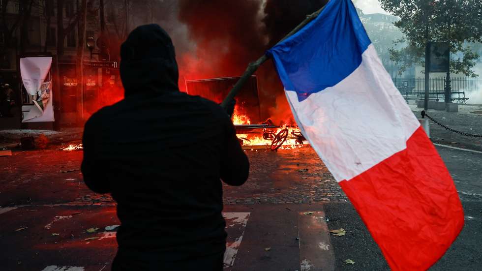 epa13312289 A protester carrying a French flag faces police at Place de la Madeleine during a demonstration against rising living costs and cuts to public services in Paris, France, 17 October 2026. The nationwide mobilization brought together Yellow Vest (Gilets Jaunes) activists, high school and university students, trade unions and other groups protesting rising living costs, fuel prices and deteriorating public services, while demanding improvements in education and school conditions.  EPA/MOHAMMED BADRA