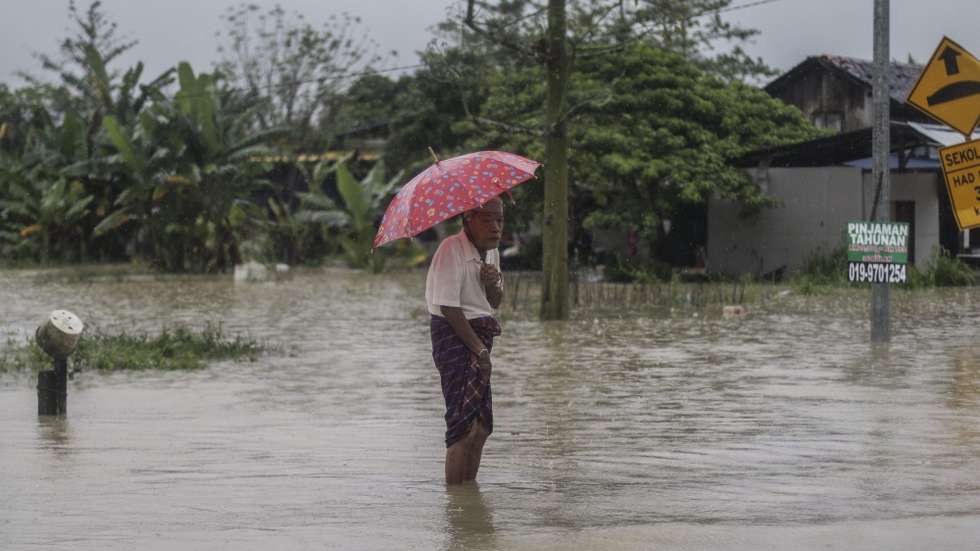 epa05695971 A man holds an umbrella as he stands on a flooded road during rain at Pasir Puteh, Kelantan, around 400km from Kuala Lumpur, Malaysia, 03 January 2016. 'There was a drastic increase in the number of evacuees in the Pasir Mas district, to 2,322 people from 936 families compared to 241 people from 85 families last night', Kelantan Civil Defence Force director Zainuddin Hussin said on 03 January.  EPA/AHMAD YUSUFI