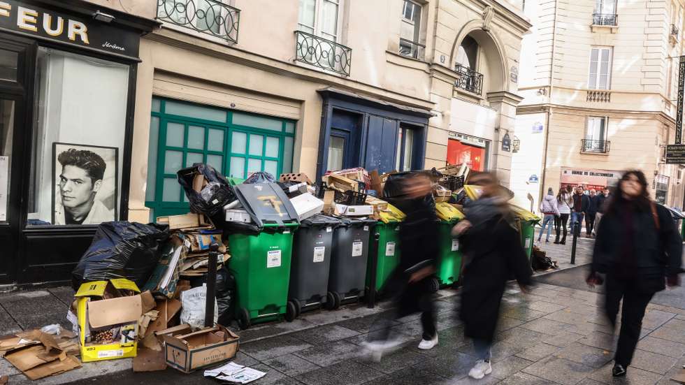 epa10522116 People pass by next to garbage cans overflowing with trash in Paris, France, 14 March 2023. Garbage collectors have joined the massive strikes in France against the government's pension reform plans, piling the streets of the French capital in the meantime with thousands of tonnes of garbage.  EPA/Mohammed Badra