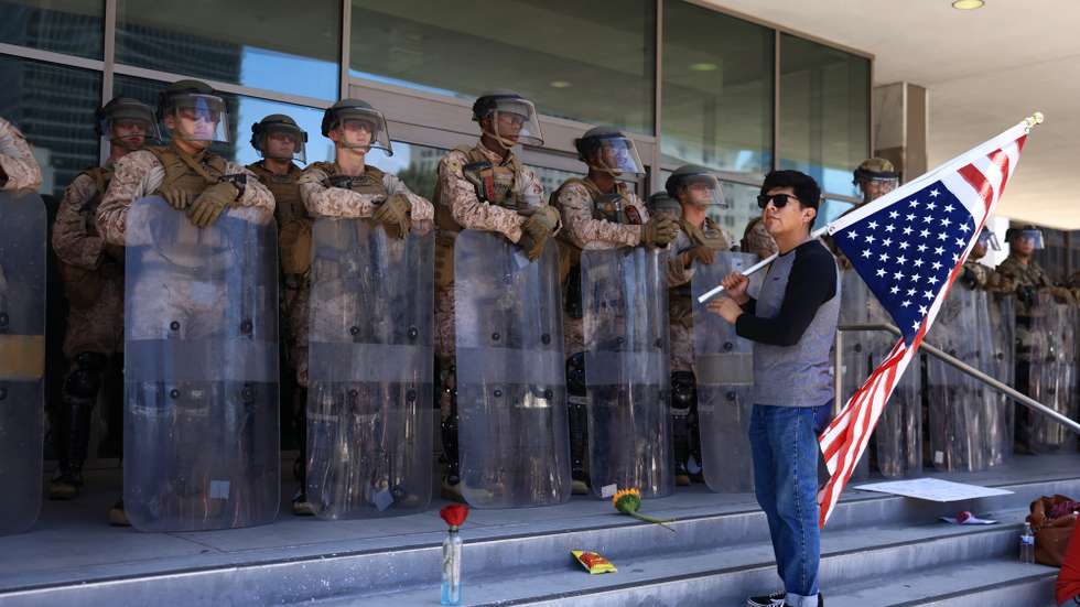 epa12216612 A protester with a US flag stands in front of US Marines guarding the Edward R. Roybal Federal Building, during an Anti-ICE protest held during the Fourth of July holiday, in Los Angeles, California, USA, 04 July 2025.  EPA/DAVID SWANSON