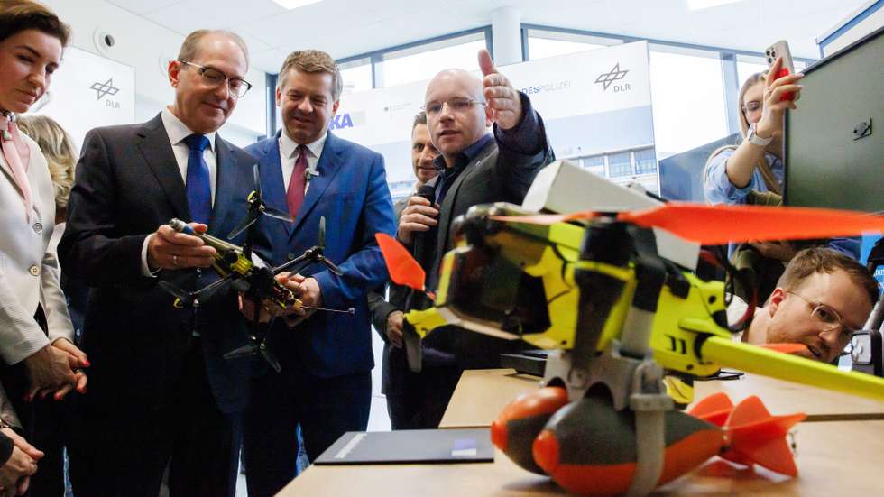 epa13177013 German Interior Minister Alexander Dobrindt (2-L), flanked by German Minister of Research, Technology and Space Dorothee Baer (L) and Saxony-Anhalt State Premier Sven Schulze (3-L), receives explanations on drones with fake explosive add-ons during the inauguration of a new drone safety technology center at the DLR site in Cochstedt district of Hecklingen, Germany, 18 August 2026. The newly opened drone security research center aims to enhance the safety and resilience of unmanned aerial systems, following an early-August 2026 incident where an explosive-laden drone was discovered near active runways at Leipzig/Halle Airport.  EPA/CLEMENS BILAN