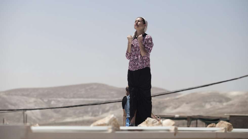 epa04205229 An Israeli settler prays on the roof of her house as she refused to step down, during a demolition operation in the West Bank illegal settlement of Maale Rehavam, on 14 May 2014. The Israeli Supreme Court rule that until 18 May the illegal structures in the settlements of Ma'aleh Rehavam, Ramat Gilad, and Givat Asaf need to evacuate because they are erected on Palestinians private land.  EPA/ABIR SULTAN