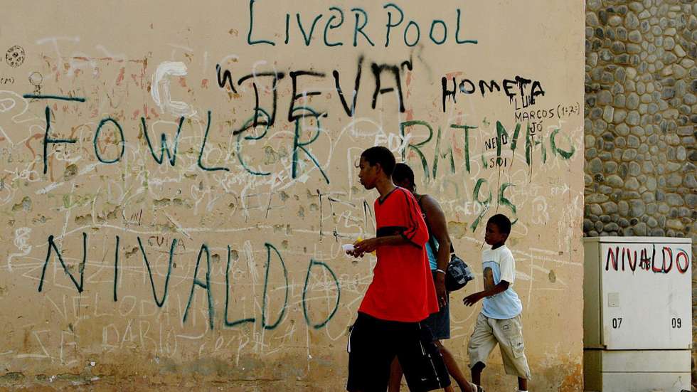epa000241191 Cape Verdians walk past graffiti refering to British and Brazilian footballers in the Platau area of Praia on the island of Santiago, Cape Verde Wednesday 28 July 2004. Portugese mariners first landed on th Cape Verde islands in 1456 and today it is the only country in the West Africa region with a population of primarily mixed European and African descent. The Brazilian president, Lula da Silva is currently visiting the islands and is meeting with businessmen to encourage development.  EPA/NIC BOTHMA
