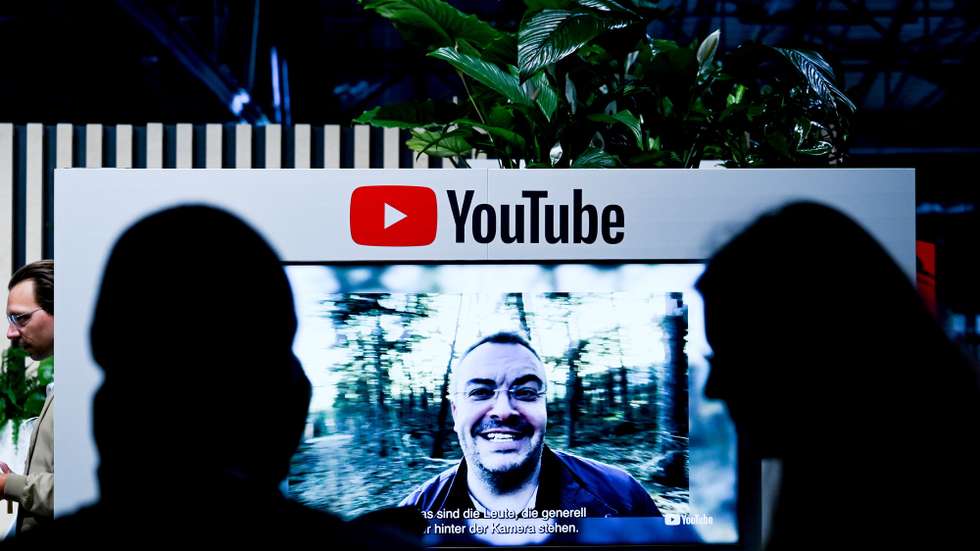epa10004040 Visitors next to a screen with YouTube logo at the 're:publica 22’ digital conference in Berlin, Germany, 09 June 2022. The 're:publica' is one of the largest conferences about digital culture, blogs, social media and information society in the world. It takes place annually in Berlin and runs from 08 to 10 June.  EPA/FILIP SINGER
