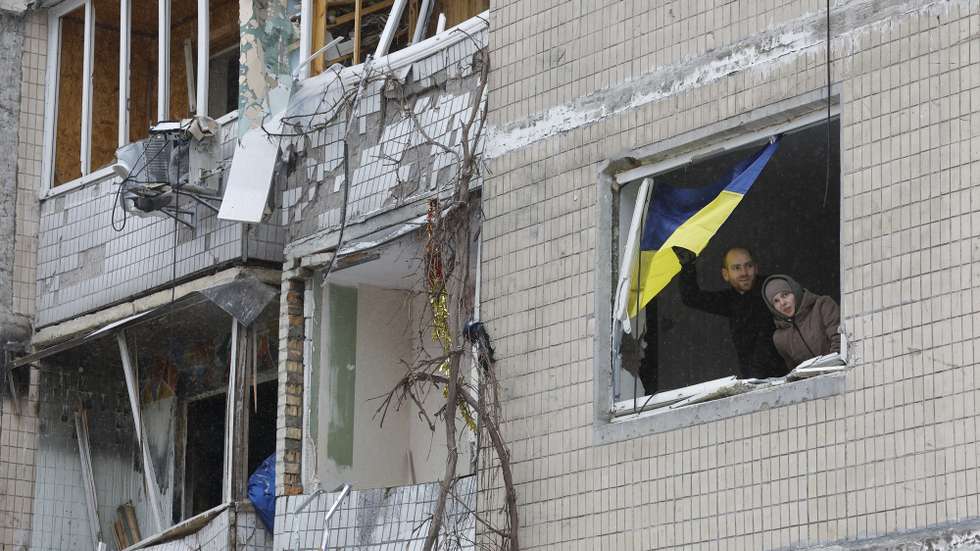 epa11055046 Locals stand by a window with a national flag as they look out from their damaged flat at the site of a damaged building a day after a missile strike, in Kyiv (Kiev), Ukraine, 03 January 2024, amid the Russian invasion. At least 27 people were hospitalized and an injured elderly woman died in an ambulance after a fire broke out in a multi-story building as a result of a rocket attack in Kyiv on 02 January 2024, the city mayor Vitali Klitschko wrote on telegram. Some 130 residents were evacuated from the burning building, the State Emergency Service said.  EPA/SERGEY DOLZHENKO