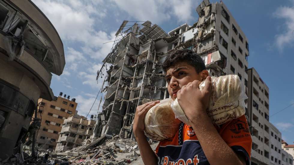 epa10922257 A Palestinian youth carrying bread walks past buildings destroyed in recent Israeli strikes in Al Remal, in Gaza City, 16 October 2023. Israel has warned all citizens of the Gaza Strip to move to the south ahead of an expected invasion. More than 2,750 Palestinians and 1,400 Israelis have been killed according to the Israel Defense Forces (IDF) and Palestinian Health Ministry after Hamas militants launched an attack against Israel from the Gaza Strip on 07 October.  EPA/MOHAMMED SABER
