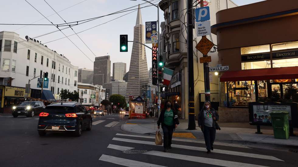 epa08853920 Pedestrians walk across a street in North Beach, as the Transamerica Pyramid building looms in the background, in San Francisco, California, USA, 30 November 2020. San Francisco is preparing for the most restrictive COVID-19 reopening tier (Purple), joining other Bay Area counties in a California curfew prohibiting non-essential business and personal gatherings from 10pm to 5am to help stop the spread the coronavirus, as the state is seeing the high rates of positive cases and hospitalizations.  EPA/JOHN G. MABANGLO