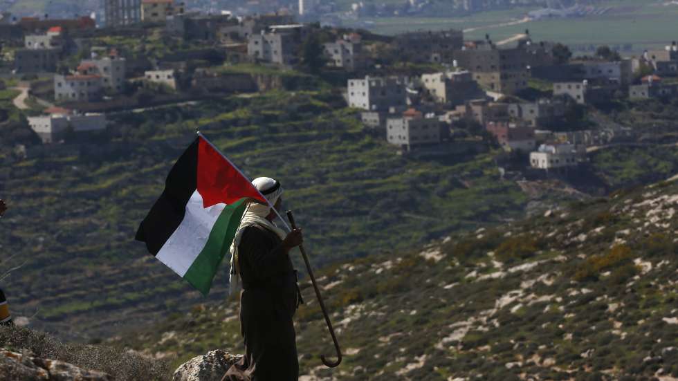 epa09038334 A Palestinian man waves Palestine flag during a demonstration against Israel's settlements in the village of Bet Dajan near the northern West Bank city of Nablus, 26 February 2021.  EPA/ALAA BADARNEH