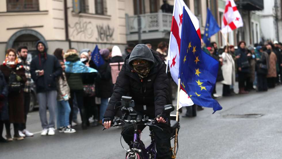 epa11796068 A protester rides a bicycle with EU and Georgian flags near supporters of the Georgian opposition during a protest action in Tbilisi, Georgia, 28 December 2024. Georgian lawmakers elected Mikheil Kavelashvili as the country's new president on 14 December in a controversial parliamentary vote that sparked accusations of illegitimacy and protests. Kavelashvili will be inaugurated as President of Georgia on 29 December 2024.  EPA/DAVID MDZINARISHVILI