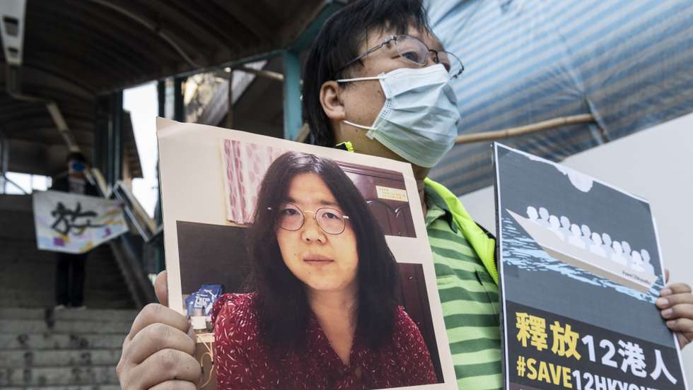 epa08907258 A pro-democracy activist stands near the Liaison Office of the Central People's Government in the Hong Kong Special Administrative Region department as he holds up a signs in support of Chinese citizen journalist Zhang Zhan who has been sentence to four years in prison and the 12 arrested people in China in Hong Kong, China, 28 December 2020. The 12 people have been detained for over 130 days after they were intercepted at the sea in August as they allegedly tried to flee from Hong Kong to Taiwan by speedboat.  EPA/MIGUEL CANDELA