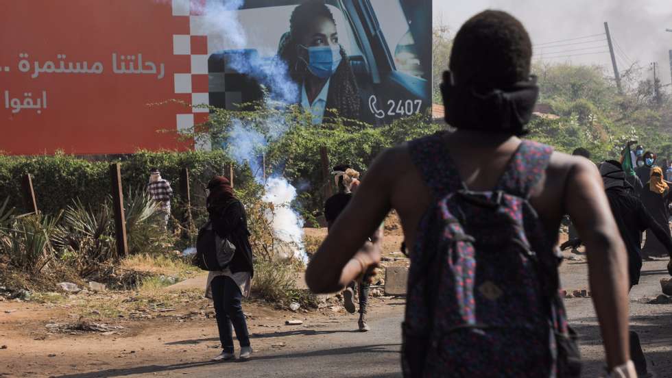 epa09676048 Sudanese protesters run for cover as security forces fire tear gas near an advertising billboard reading in Arabic &#039;our journey continues&#039; during an anti-coup protest, in Khartoum, Sudan, 09 January 2022. Security forces fired tear gas to disperse protesters gathering in Khartoum and attempting to march towards the presidential palace, as part of the continuing protesting movement against a military coup in October 2021. The protest was organized a day after the UN envoy for Sudan said the international group will invite different parties for talks in Sudan to end the crisis.  EPA/STRINGER