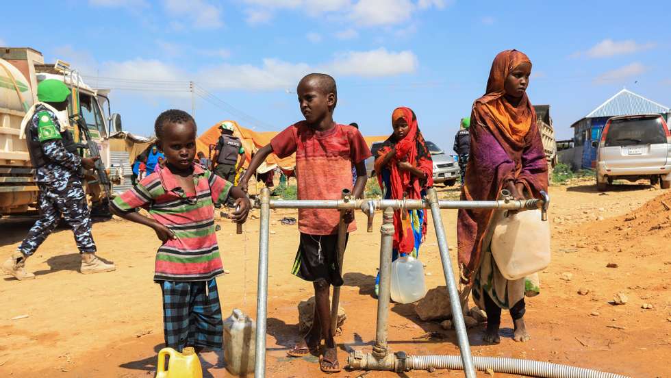 epa08078824 Children fetch water using jerry cans at a water point set up by Somalia Humanitarian Fund (SHF), as Nigerian troops (L), under the Africa Union, patrol escorting journalists and aid workers visiting people displaced by floods at an Internally Displaced Persons (IDP) camp in Belet Weyne, Hirshabelle state, some 350 kilometres north of the capital Mogadishu, Somalia, 14 December 2019 (issued 18 December 2019). At least 110,000 people have been displaced after Shabelle river burst its banks in late October 2019 following heavy rains in the region. According to the United Nations Office for the Coordination of Humanitarian Affairs (UN OCHA) in Somalia, the rains have inundated 207,000 hectares of land along Shabelle and Juba rivers, raising concerns about food security.  EPA/DANIEL IRUNGU