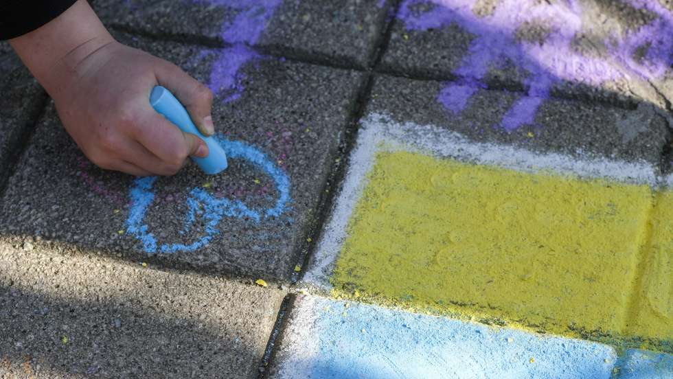 epa09812096 A child paints the Ukrainian flag and a heart on the ground as people who fled Ukraine to Belgium after Russia's invasion of Ukraine wait outside an immigration office in Brussels, Belgium, 09 March 2022. A temporary reception center for people who fled Ukraine has been set up in Brussels to complete immigration formalities.  EPA/OLIVIER HOSLET
