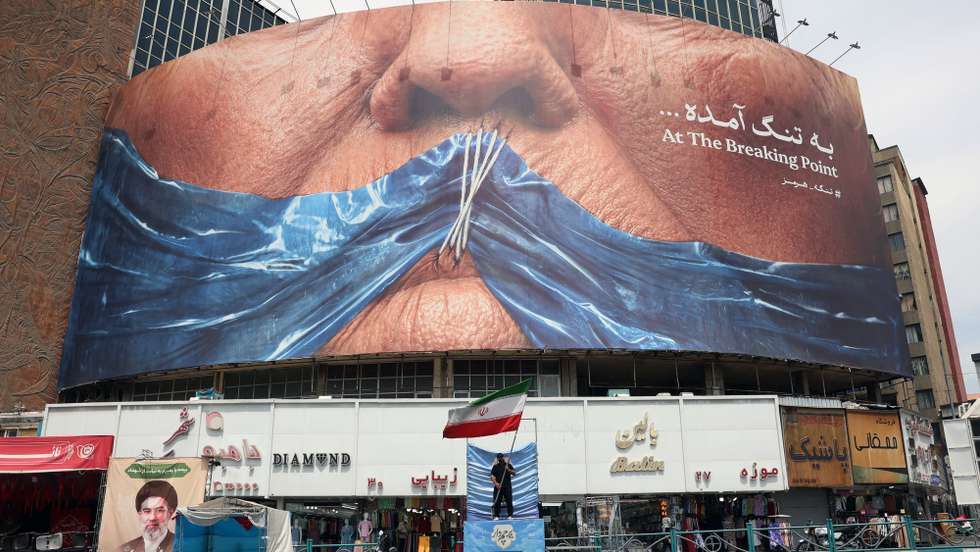 epa12999702 A man holds Iran’s national flag in front of a large anti-US billboard featuring US President Donald Trump and the Strait of Hormuz at Valiasr Square in Tehran, Iran, 28 May 2026. US President Donald Trump recently announced that a potential peace agreement to end the conflict and reopen the Strait of Hormuz has been largely negotiated through Pakistani mediators. However, the US has since launched new strikes in southern Iran.  EPA/ABEDIN TAHERKENAREH RESTRICTIONS: NO Access Israel Media/Persian Language TV Stations Outside Iran/Strictly No Access BBC Persian/VOA Persian/Manoto TV/Iran International TV. (As mandated by Iran's Directorate General for Foreign Media) --