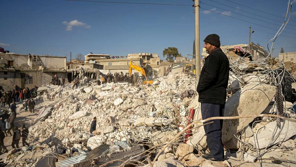 epa10455053 A man watches as rescuers and volunteers search for survivors under the rubble of collapsed houses, in Harim town near Idlib, Syria, 08 February 2023. More than 11,000 people have died and thousands more injured after two major earthquakes struck southern Turkey and northern Syria on 06 February. Authorities fear the death toll will keep climbing as rescuers look for survivors across the region.  EPA/KARAM AL-MASRI