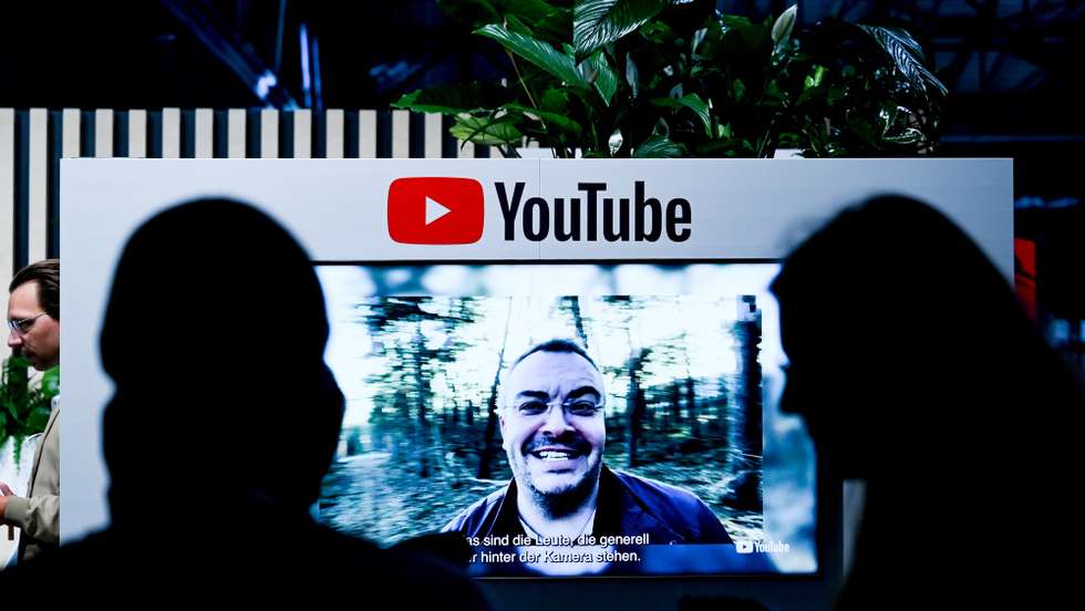 epa10004040 Visitors next to a screen with YouTube logo at the 're:publica 22’ digital conference in Berlin, Germany, 09 June 2022. The 're:publica' is one of the largest conferences about digital culture, blogs, social media and information society in the world. It takes place annually in Berlin and runs from 08 to 10 June.  EPA/FILIP SINGER