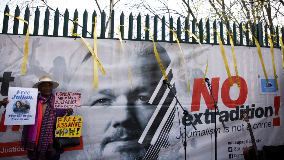 epaselect epa09844244 An activist holds placards calling for the release of Julian Assange beside a banner featuring Assange's face as well wishers gather outside HMP Belmarsh to celebrate the wedding of Stella Moris and Assange in London,  Britain, 23 March 2022.  Assange is in prison facing extradition to the United States, where he is wanted over an alleged conspiracy to obtain and disclose national defence information.  EPA/DAVID CLIFF