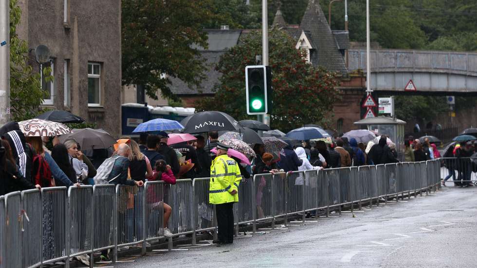 epa10178518 People queue to lay flowers at Holyroodhouse in Edinburgh, Scotland, Britain 11 September 2022. The arrival of the hearse carrying Queen Elizabeth II marks the first stage of the journey towards London. Britain's Queen Elizabeth II died at her Scottish estate on 08 September 2022.  EPA/ADAM VAUGHAN
