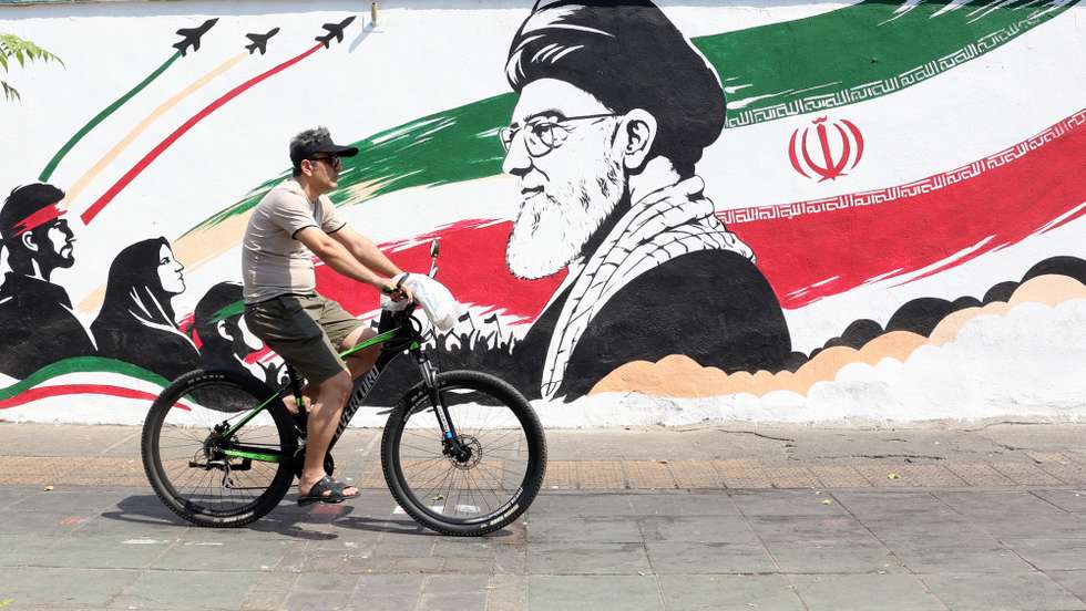 epa13165935 An Iranian man passes with his bike next to a wall painting featuring late Iranian supreme leader Ayatollah Ali Khamenei in a street in central Tehran, Iran, 13 August 2026. Tensions between Iran and the US remain high as opposing claims persist over shipping control in the Strait of Hormuz.  EPA/ABEDIN TAHERKENAREH RESTRICTIONS: NO Access Israel Media/Persian Language TV Stations Outside Iran/Strictly No Access BBC Persian/VOA Persian/Manoto TV/Iran International TV. (As mandated by Iran's Directorate General for Foreign Media) --