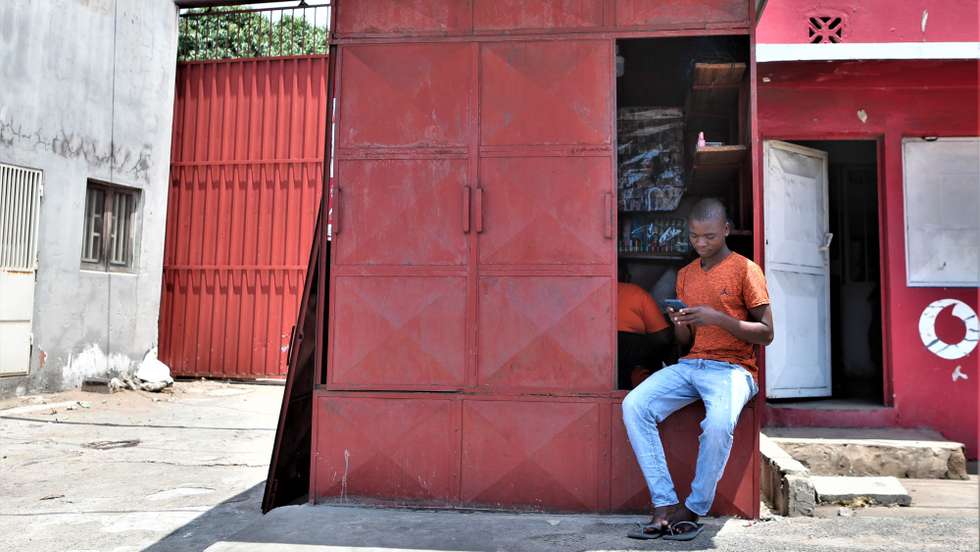 Ivan Durão, 29 anos, olha para o seu telemóvel, sentado na sua barraca com a porta entreaberta, onde faz as unhas das clientes, devido à paralisação convocada pelo candidato presidencial Venâncio Mondlane, na avenida Julius Nyerere, em Maputo, Moçambique, a 31 de outubro de 2024. A polícia moçambicana enviou esta madrugada mensagens escritas para os telemóveis (SMS) pedindo à população que se abstenha de “práticas criminosas”, no primeiro dia de uma greve geral de uma semana convocada pelo candidato presidencial Venâncio Mondlane. LUÍSA NHANTUMBO/LUSA