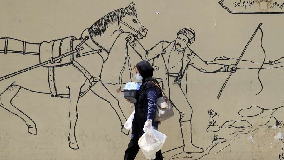 epa10686680 An Iranian woman carries her belongings as she walks next to a wall painting in a street in Tehran, Iran, 12 June 2023. Iran's Supreme Leader Ali Khamenei said on 11 June during a meeting with Iranian nuclear scientists, that the West could not stop Iran's nuclear progress, as he urged continued cooperation with the International Atomic Energy Agency (IAEA), amidst the scrutiny from Western powers on the country's nuclear programme.  EPA/ABEDIN TAHERKENAREH