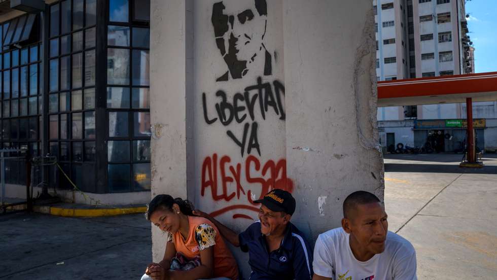 epa08990282 Several people is sitting next to a wall with graffiti demanding the release of Alex Saab, in Caracas, Venezuela, 05 February 2021. The Court of Justice of the Economic Community of West African States (ECOWAS) held on 05 February a hearing on the extradition case of Ãlex Saab, alleged front man of the President of Venezuela, NicolÃ¡s Maduro, arrested in Cape Verde and claimed by the US for alleged money laundering.  EPA/MIGUEL GUTIERREZ