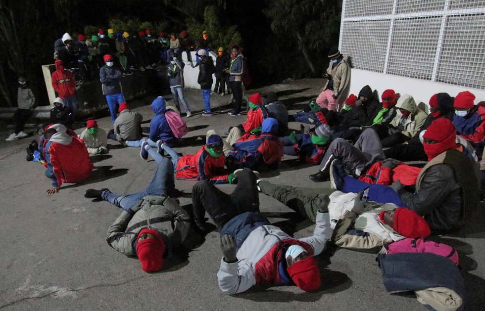 epa09647672 Several sub-Saharan migrants stage a sit-in protest outside Temporary Migrant Shelter (CETI) in Ceuta, Spanish enclave in northern Africa, early 18 December 2021. They staged the protest after some one hundred of them left the center to protest as they are stayed at the center much time and they are prevented from traveling to Spanish mainland.  EPA/Reduan