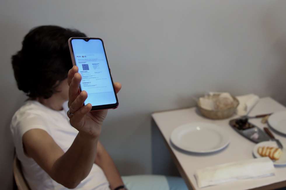 Cliente exibe o certificado digital no interior de um restaurante em Lisboa, após o Governo decreta que os restaurantes em concelhos de risco elevado ou muito elevado – um total de 60 – passam a ter de exigir certificado digital ou teste negativo à covid-19 a partir das 19:00 de sexta-feira e aos fins de semana para refeições no interior, Lisboa, 10 de julho de 2021. As pessoas em esplanadas que precisarem de entrar nos restaurantes para acesso aos serviços comuns, como instalações sanitárias, ou para efetuarem pagamento, estão dispensadas de apresentar um teste negativo à covid-19 ou o certificado digital. MANUEL DE ALMEIDA/LUSA