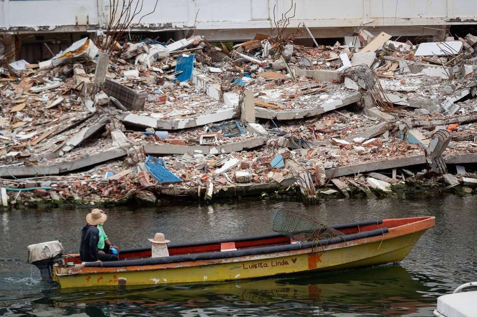 epa13158504 A person rides a boat beside a collapsed building in La Guaira, Venezuela, 09 August 2026. La Guaira is the state hardest hit by the two earthquakes that struck Venezuela on 24 June.  EPA/RONALD PENA R